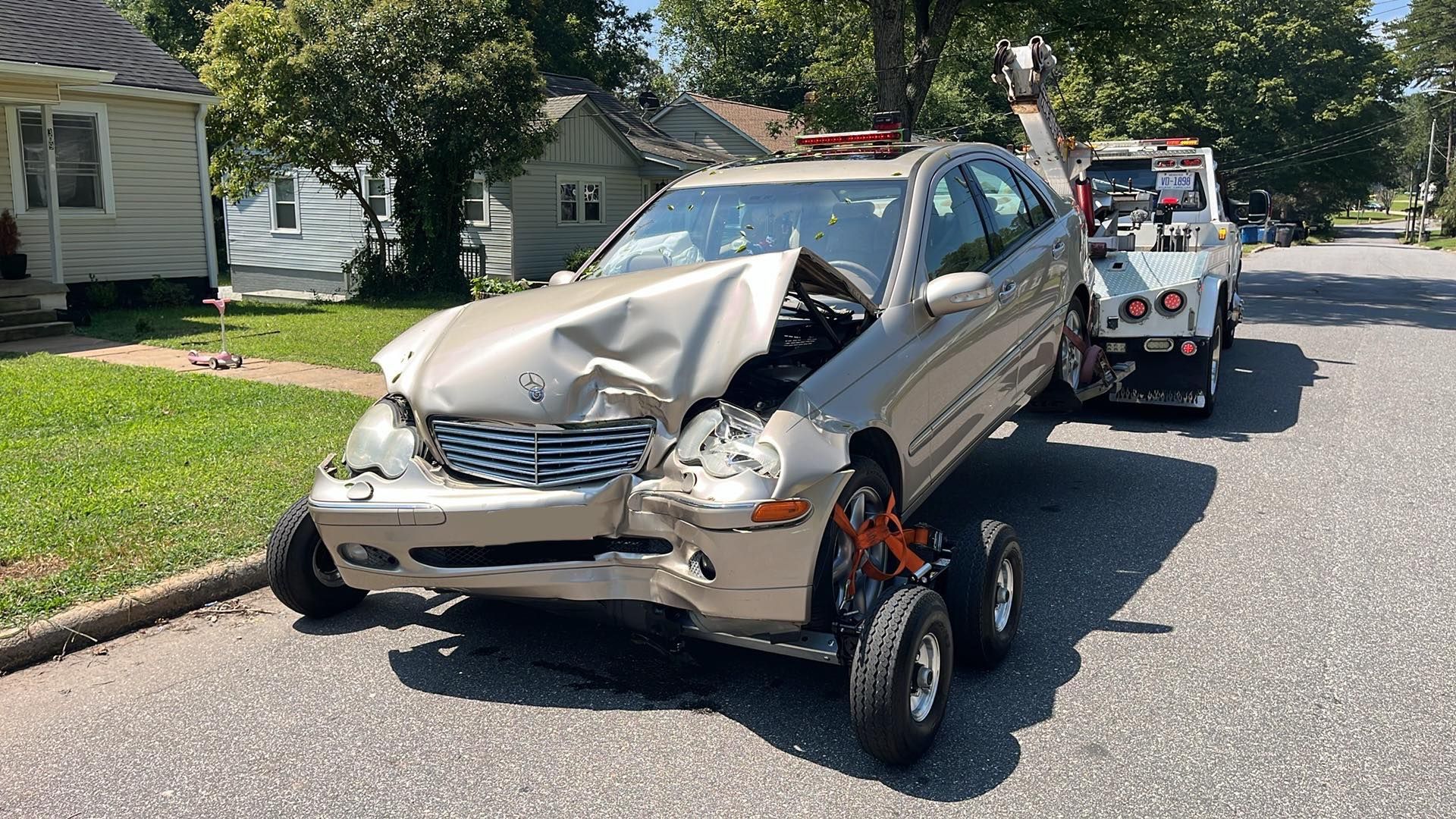 Damaged beige car being towed away after a collision on a residential street.