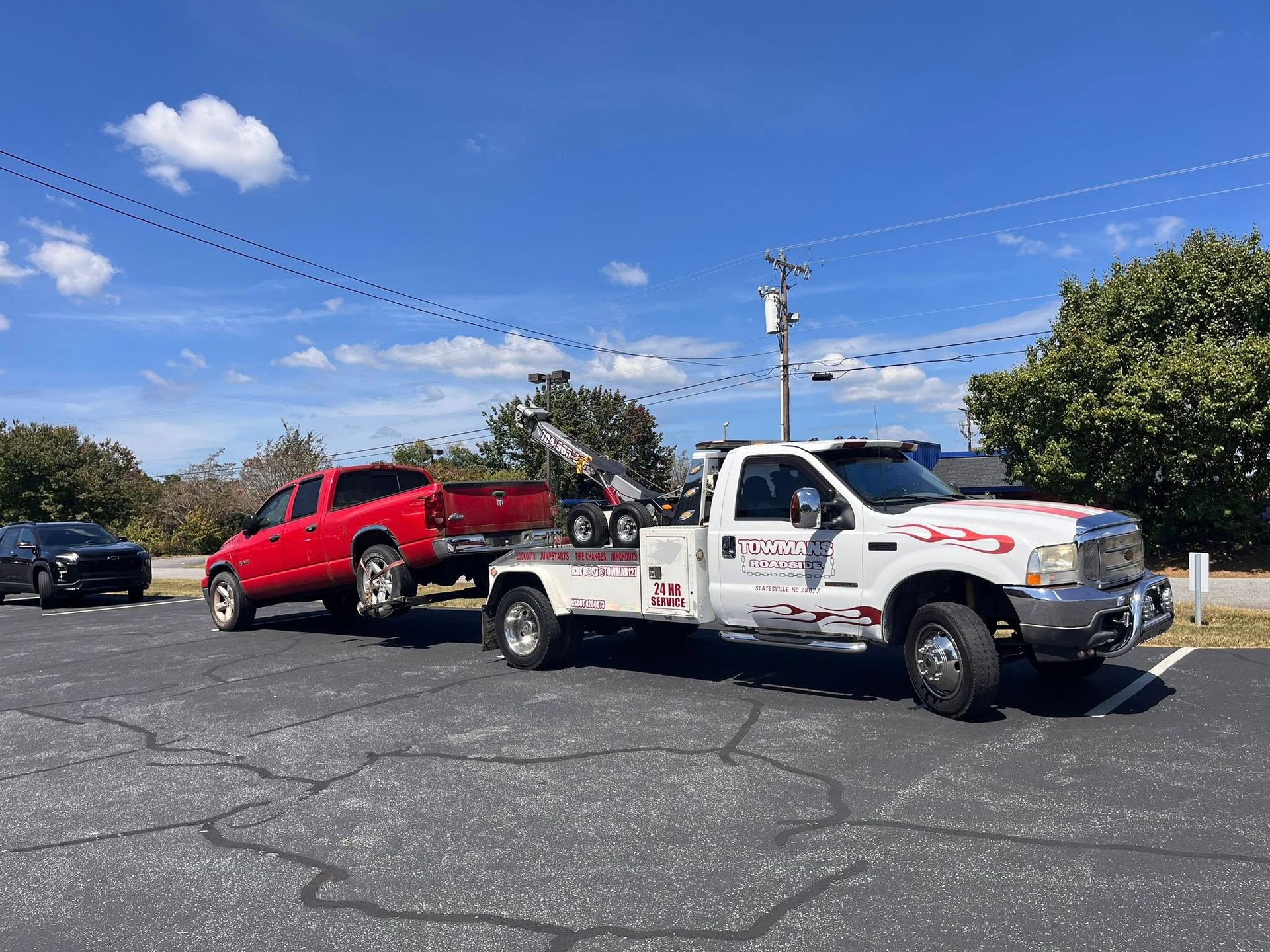 Tow truck towing a red pickup truck in a parking lot on a sunny day.