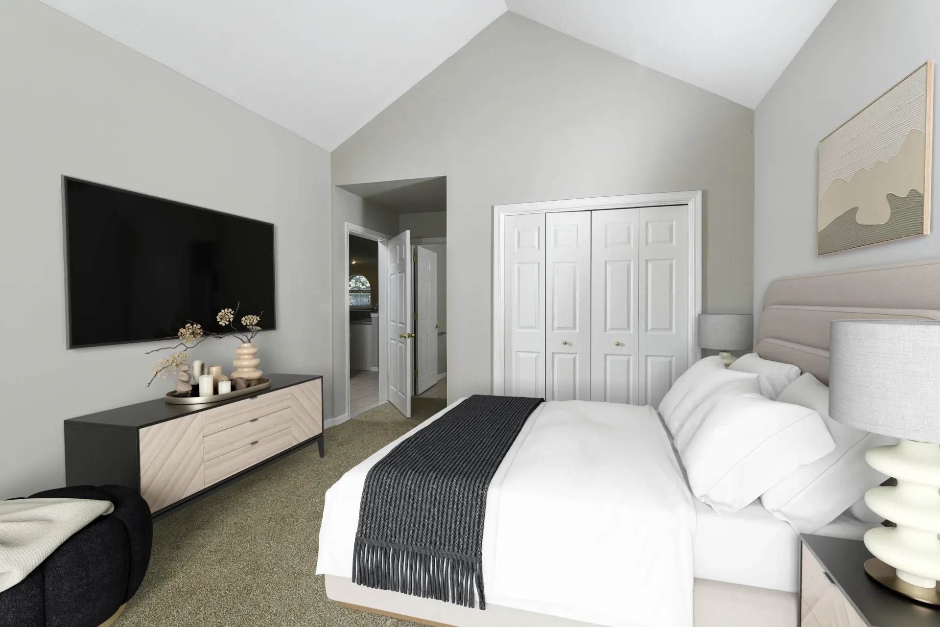 Bedroom with a large bed, dresser, wall-mounted TV, and double closet doors at Springhouse Townhomes in Allentown, PA.