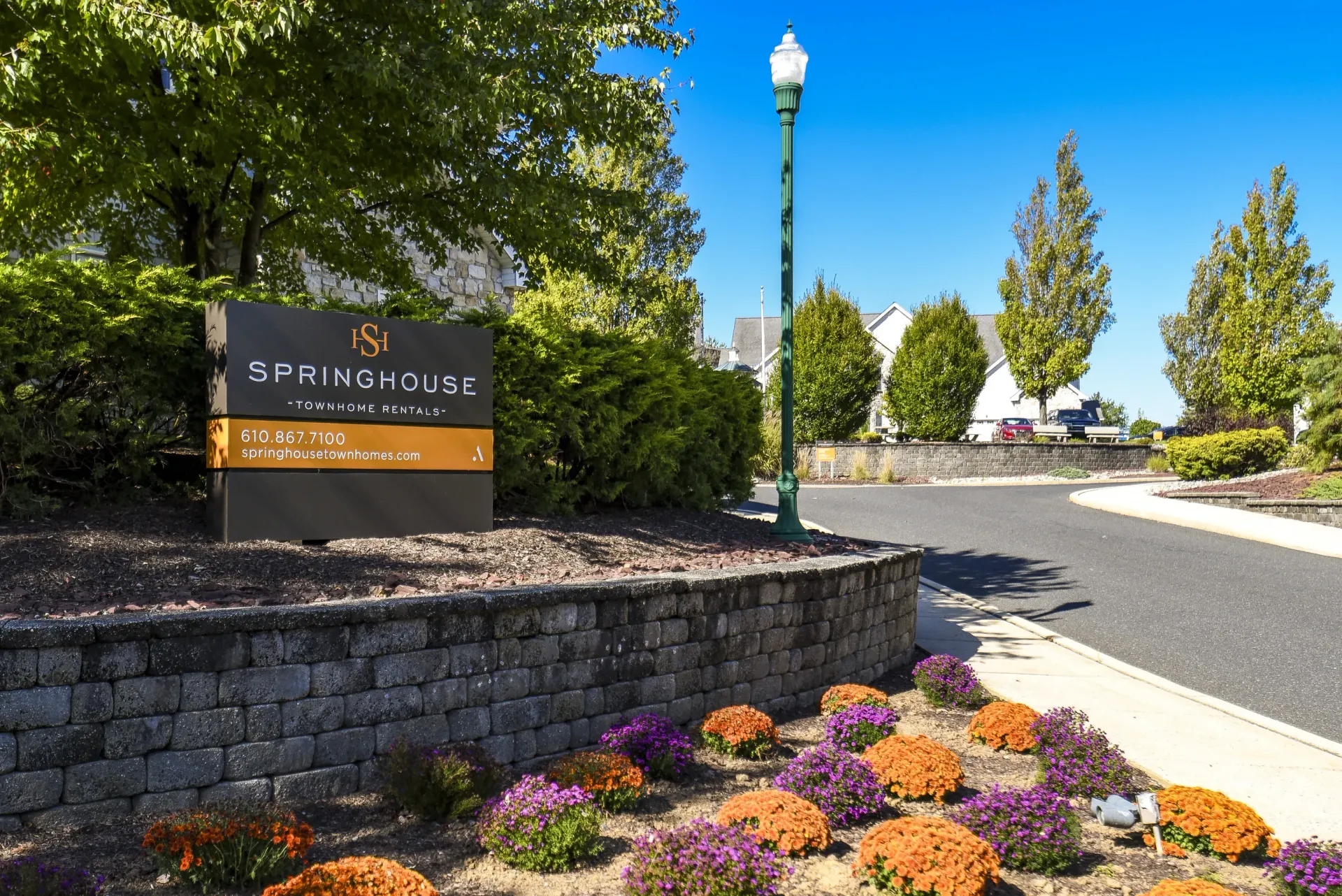 Exterior view of a townhouse community entrance sign with landscaping and a curved driveway at Springhouse Townhomes in Allentown, PA.