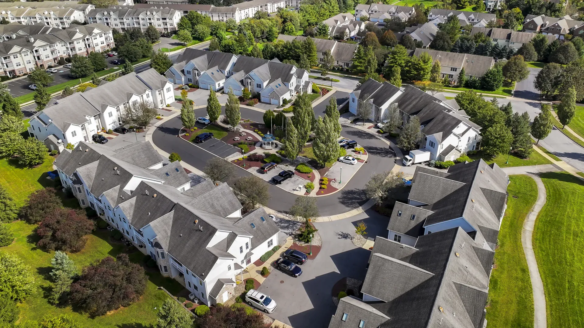 Aerial view of a suburban apartment community with white buildings, circular drive, and central gazebo at Springhouse Townhomes in Allentown, PA.