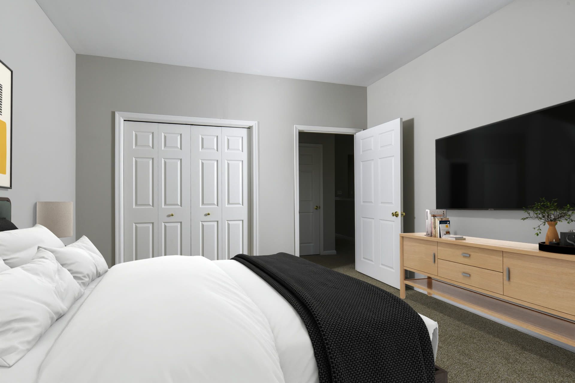 Bedroom with a neatly made bed, gray walls, double closet doors, and a TV on a wooden dresser at Springhouse Townhomes in Allentown, PA.