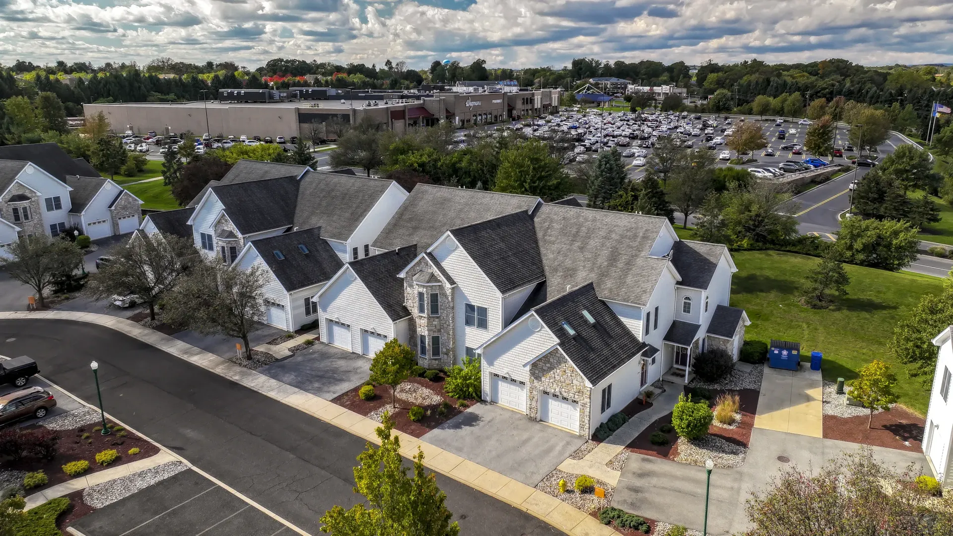 Aerial view of a suburban apartment community with white townhomes, garages, and a large parking lot at Springhouse Townhomes in Allentown, PA.