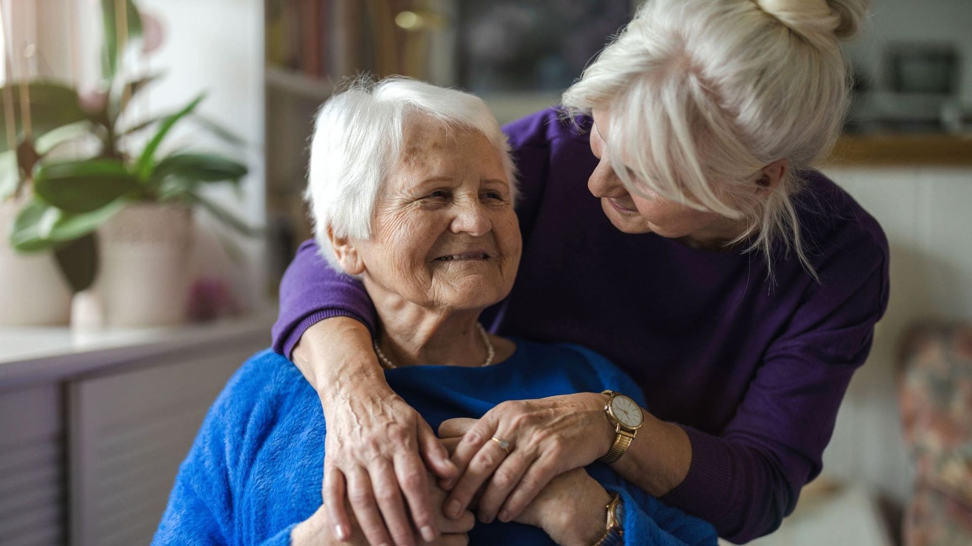 A woman is hugging an older woman in a living room.