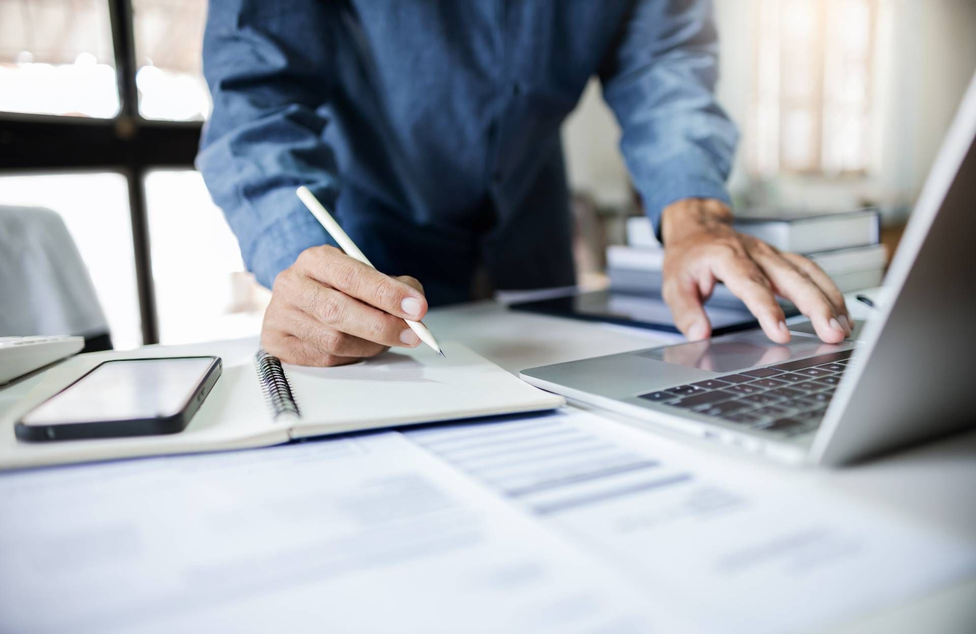 a man is writing on a piece of paper while using a laptop computer.