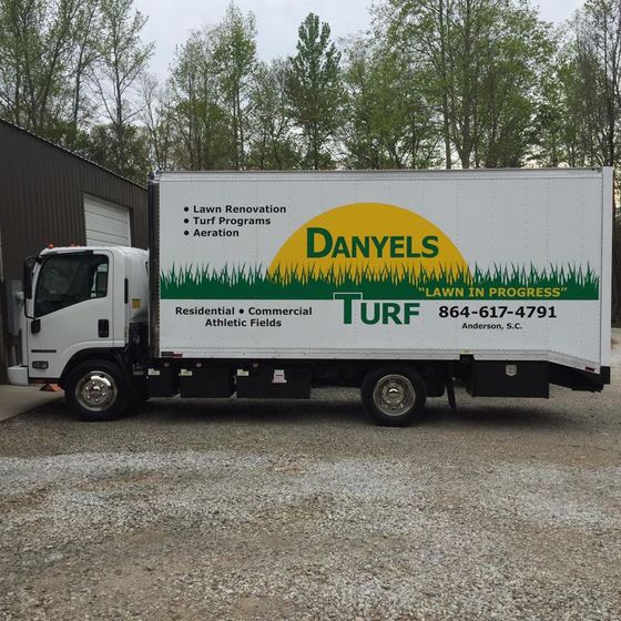 White truck with Danyels Turf logo parked outside a building.