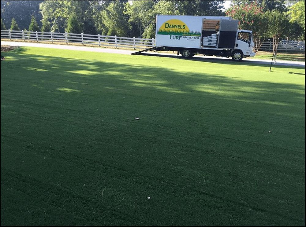 A truck with a turf logo parked on a driveway, next to a freshly laid green lawn.