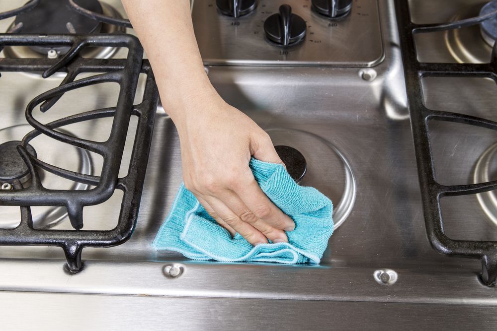 Hand Wiping a Blue Cloth Across a Stainless Steel Stovetop — Dream n Clean in Wilsonton Heights, QLD