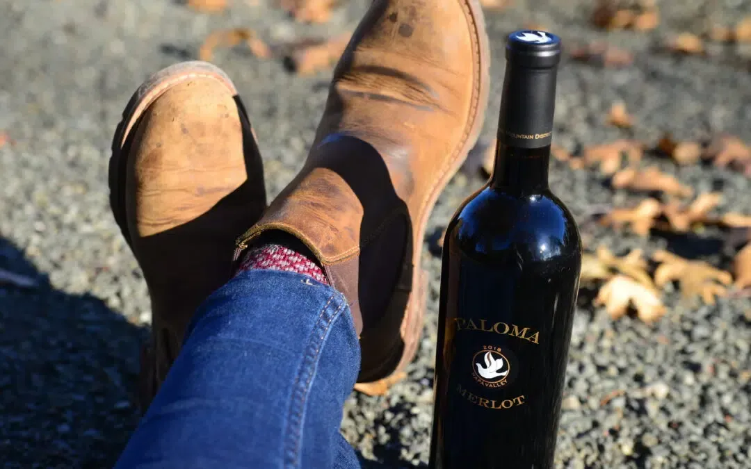 A person is laying on the ground with their feet up next to a bottle of wine.