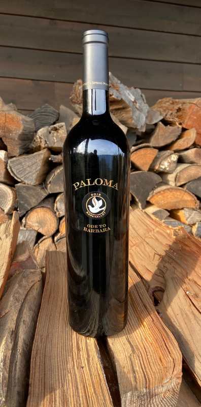 A bottle of paloma wine is sitting on top of a pile of logs.