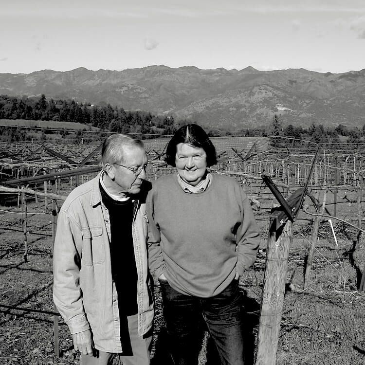 A man and a woman are standing in a field with mountains in the background