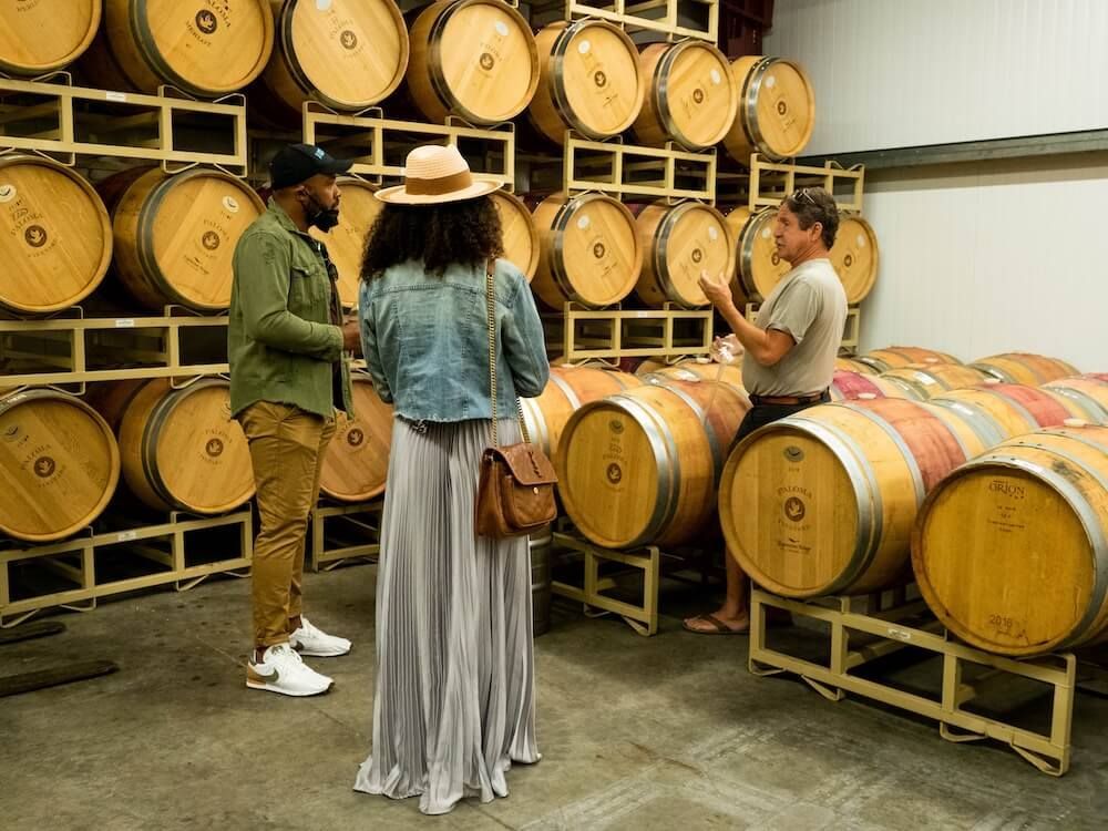 A group of people are standing in a wine cellar surrounded by wine barrels.