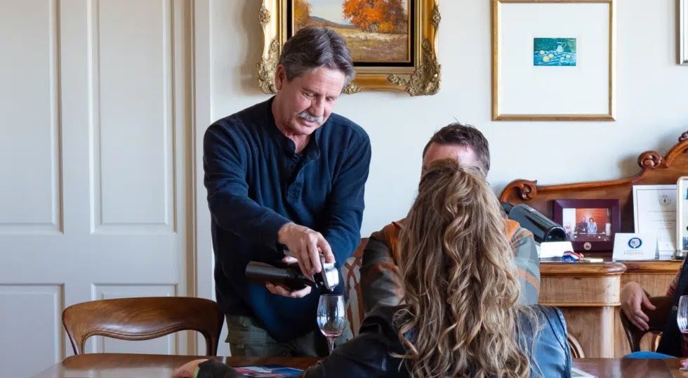A man is pouring wine into a glass for a group of people sitting at a table.