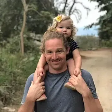 A man is carrying a little girl on his shoulders.