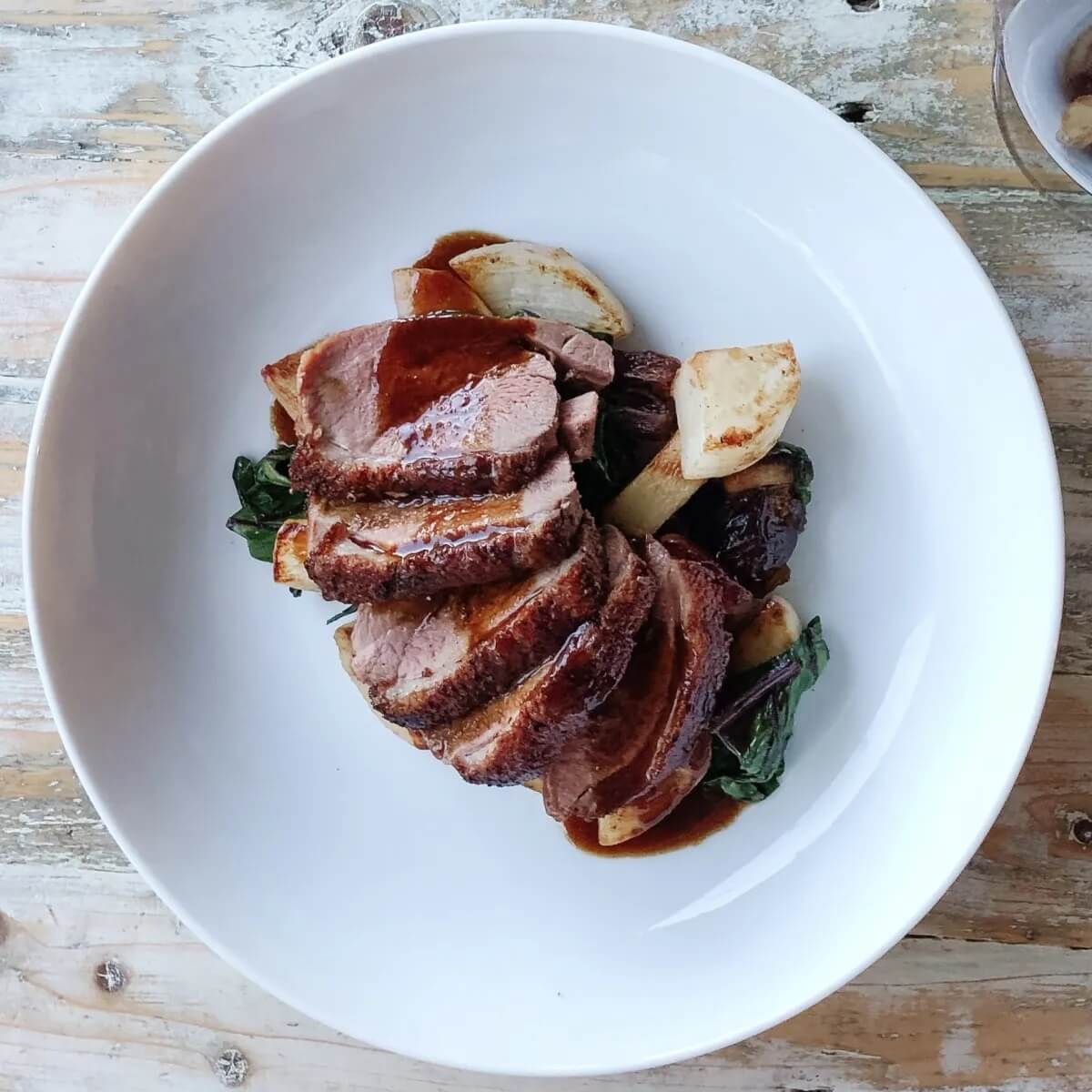 A white plate topped with meat and vegetables on a wooden table.