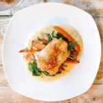 A white plate topped with a chicken and vegetables on a wooden table.