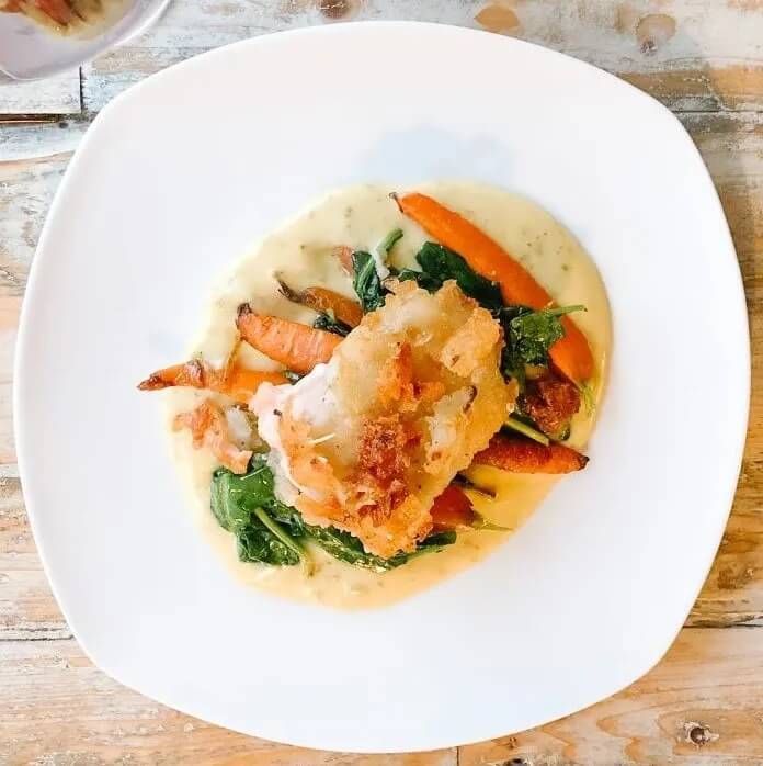 A white plate topped with a chicken and vegetables on a wooden table.