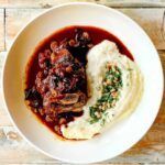 A bowl of food with mashed potatoes and sauce on a wooden table.