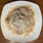 A white plate topped with spaghetti and cheese on a wooden table.