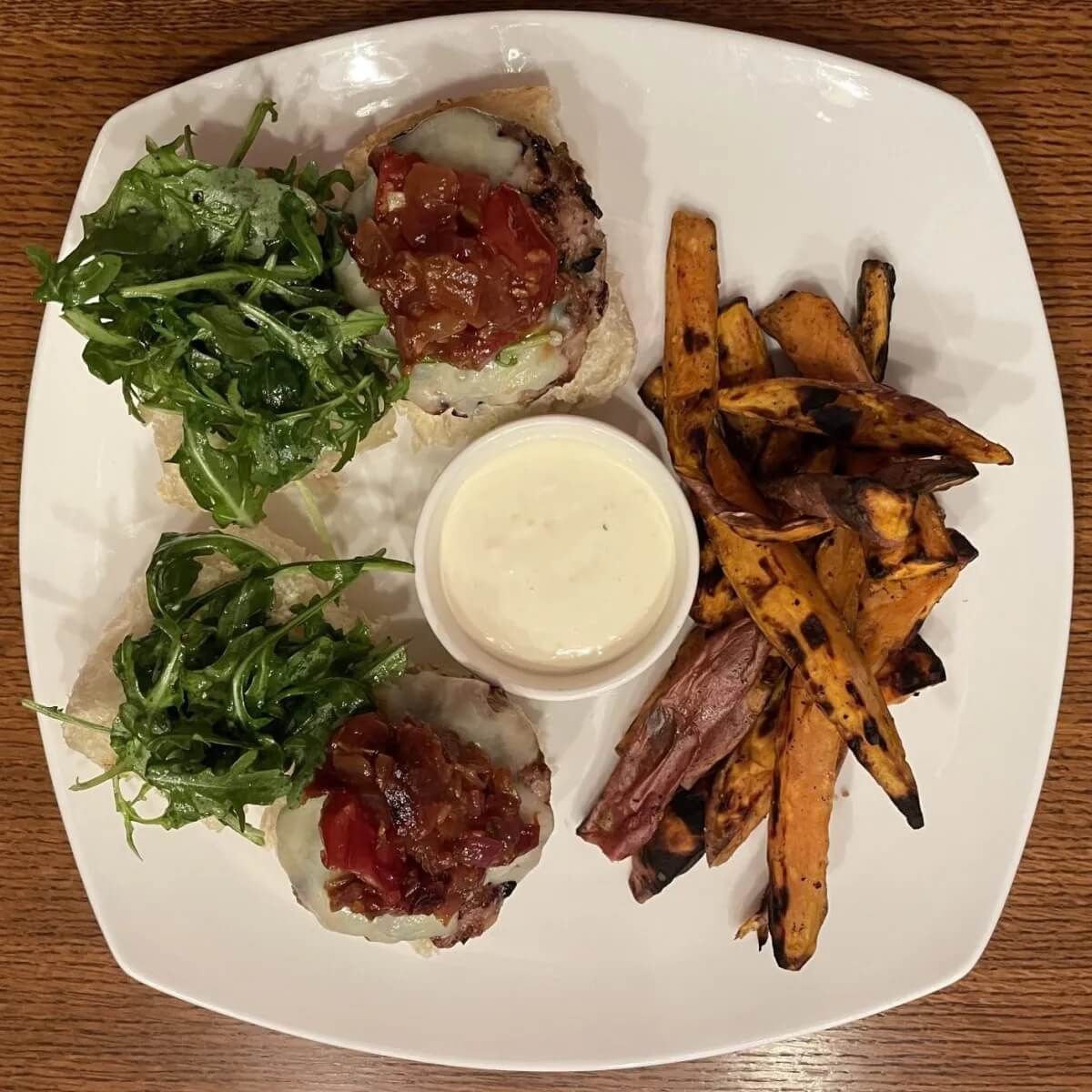 A white plate topped with meatballs , sweet potato fries , and a dipping sauce.