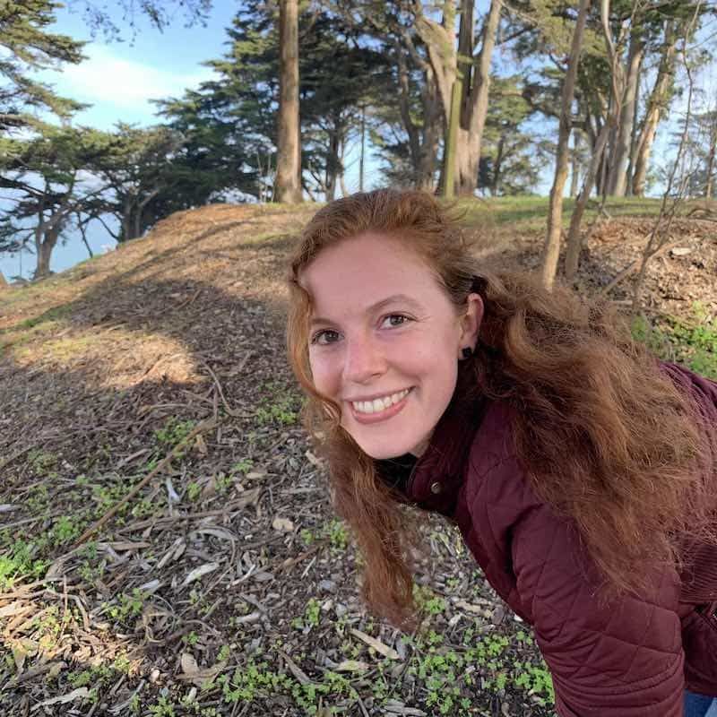 A woman is smiling while standing on top of a hill in the woods.
