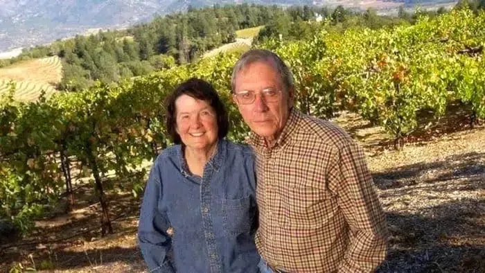 A man and a woman are posing for a picture in a vineyard.