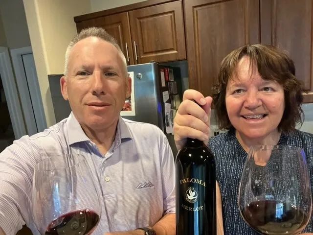 A man and a woman are holding a bottle of wine and glasses of wine.