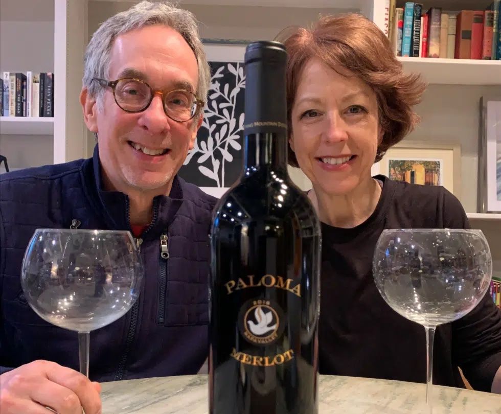 A man and woman are standing next to a bottle of paloma wine