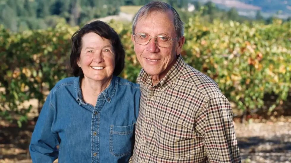 A man and a woman are posing for a picture in a vineyard.