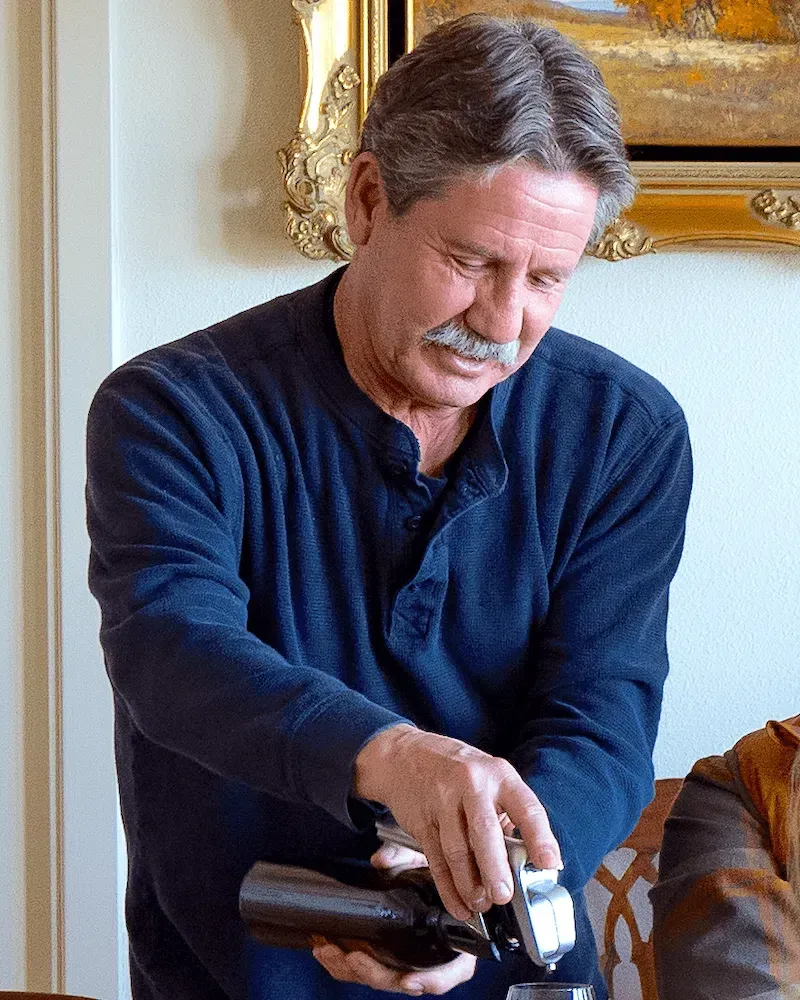 A man with a mustache is pouring wine into a glass.