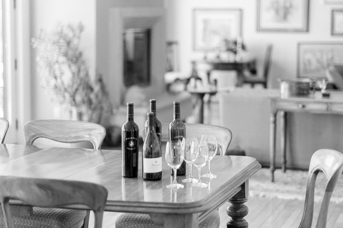 A black and white photo of a dining room table with wine bottles and glasses on it.