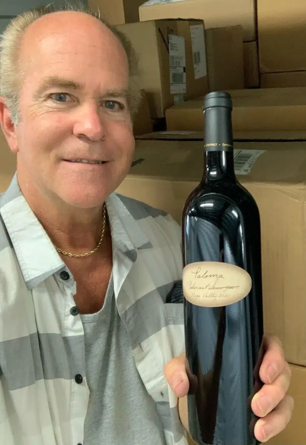 A man in a plaid shirt is holding a bottle of wine.