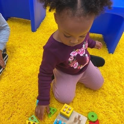 A little girl is kneeling on the floor playing with toys.