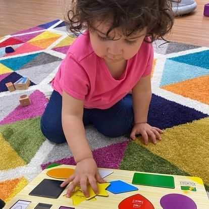 A little girl is playing with a wooden puzzle on the floor.