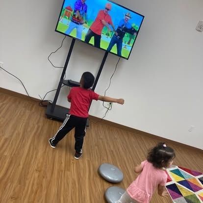 A boy and a girl are dancing in front of a television.