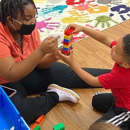A woman and a child are playing with lego blocks on the floor.