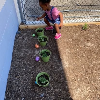 A little girl is kneeling down next to potted plants and easter eggs.