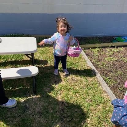 A little girl is standing in the grass holding an easter basket.