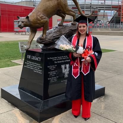 A woman in a graduation cap and gown is standing in front of a statue of a cat
