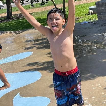Boy celebrating in the water park with arms raised.