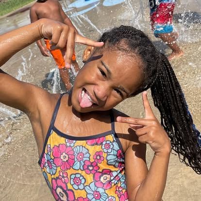 A little girl in a bathing suit is sticking her tongue out and making a peace sign.