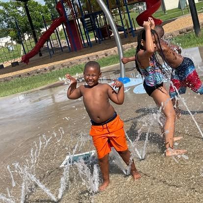 A group of children are playing in a sprinkler at a park.