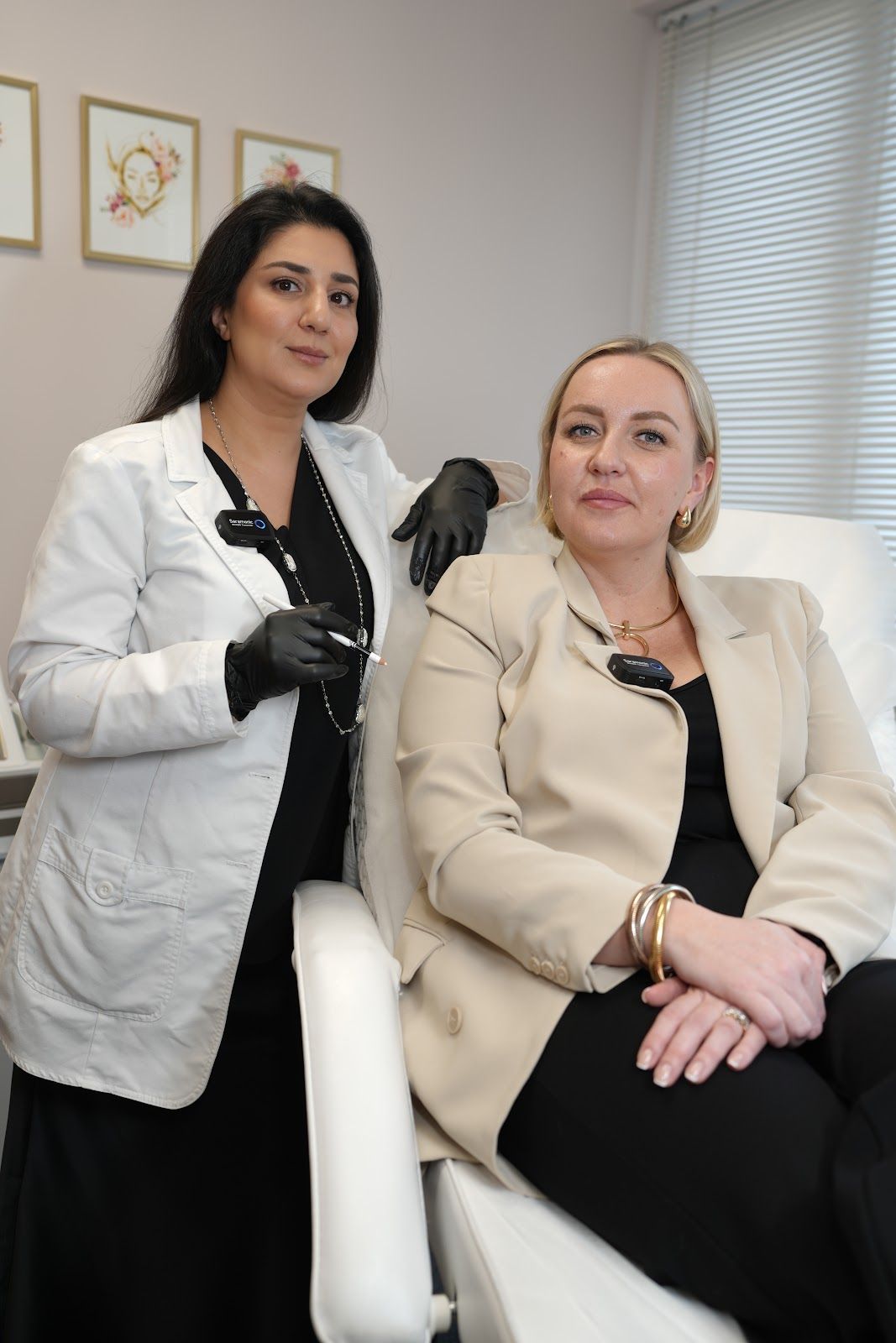 Two women in a clinic setting, one in a lab coat holding tools, the other seated, smiling.