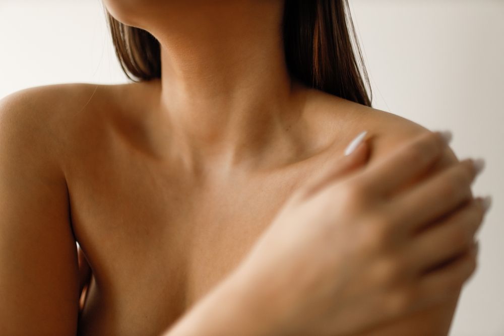 Woman's bare shoulders and upper arm; hand touches shoulder. Brown skin, white background.