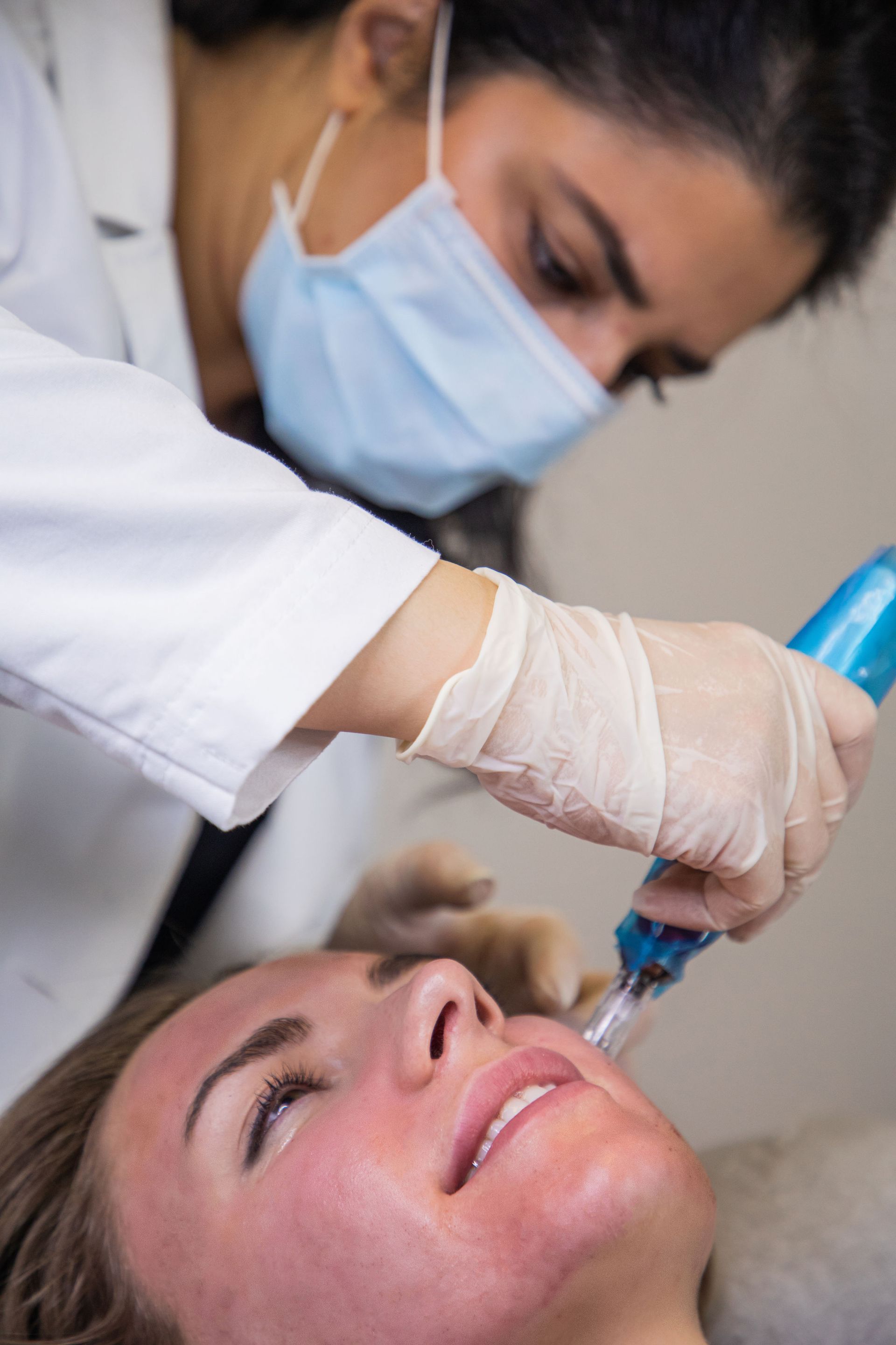 A woman is getting a treatment on her face while wearing a mask and gloves.
