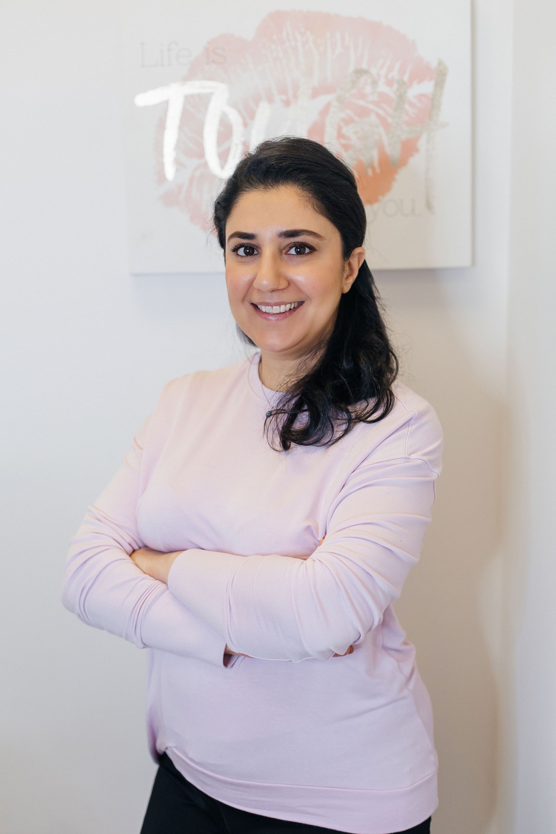 A woman in a pink sweater is posing for a picture with her arms crossed.