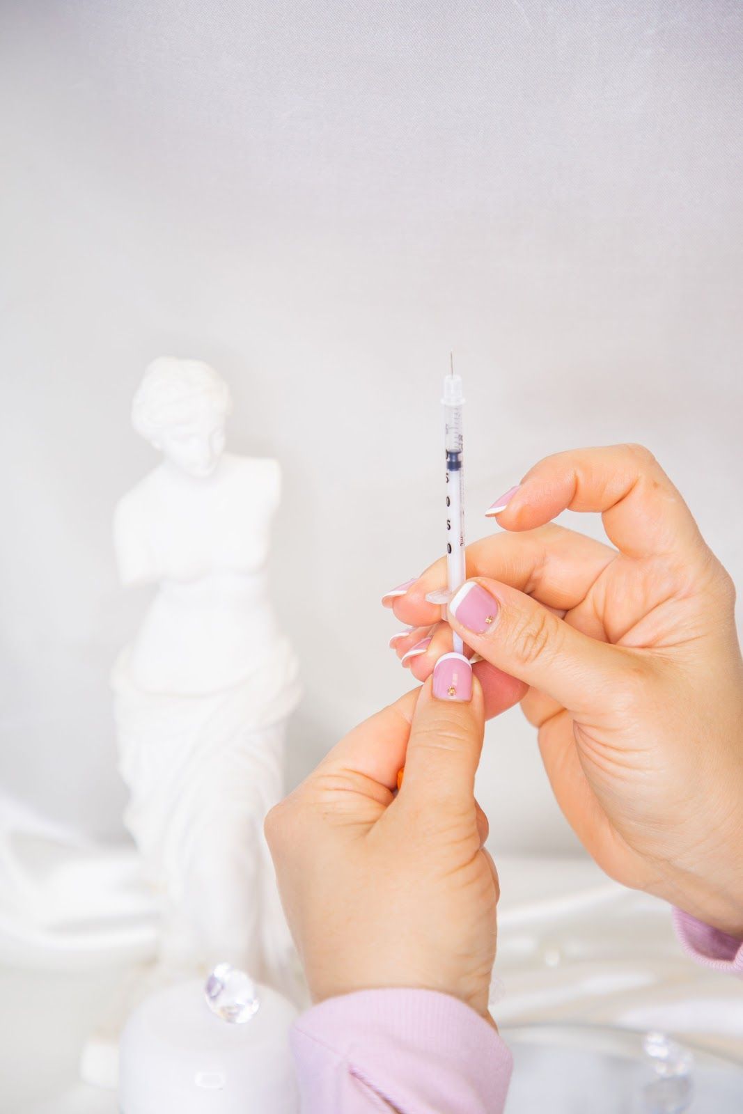 Hands holding a syringe with medication, preparing for injection. White statue in background.