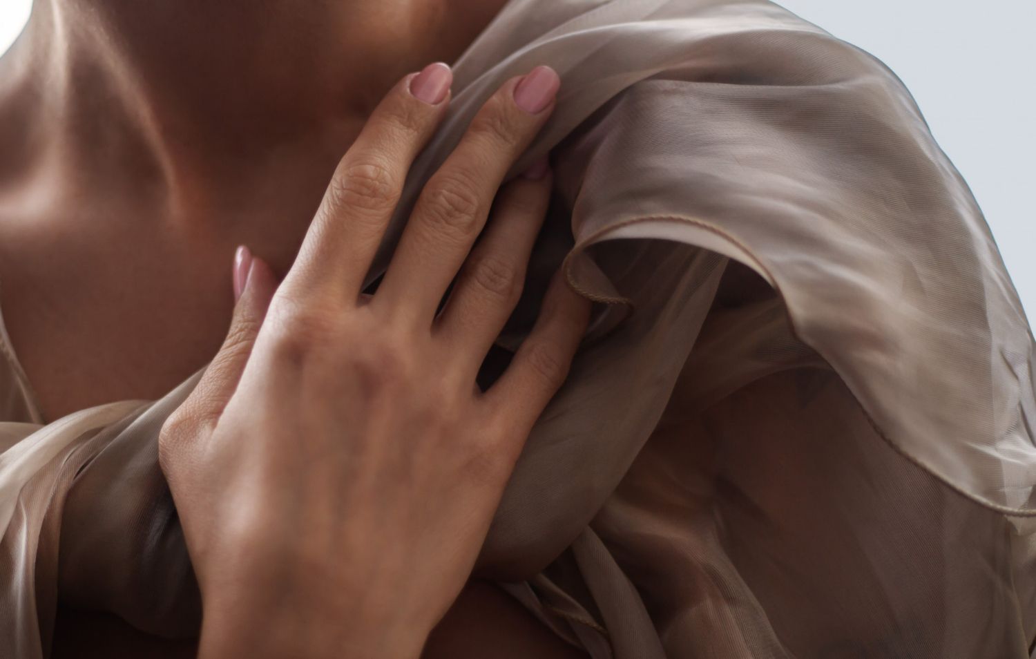 Woman's hand on her shoulder, draped with shimmering, golden fabric. Light skin, soft nails.