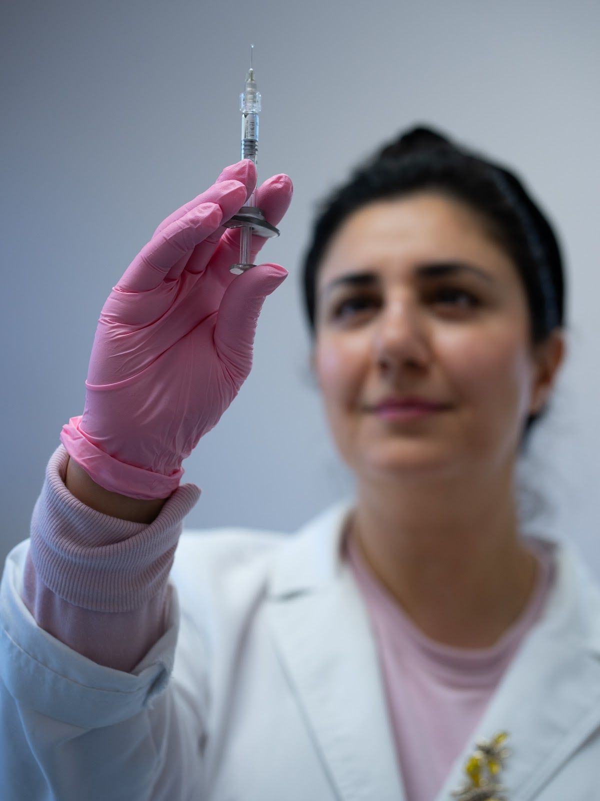 Person in pink gloves holding up a syringe, preparing an injection.
