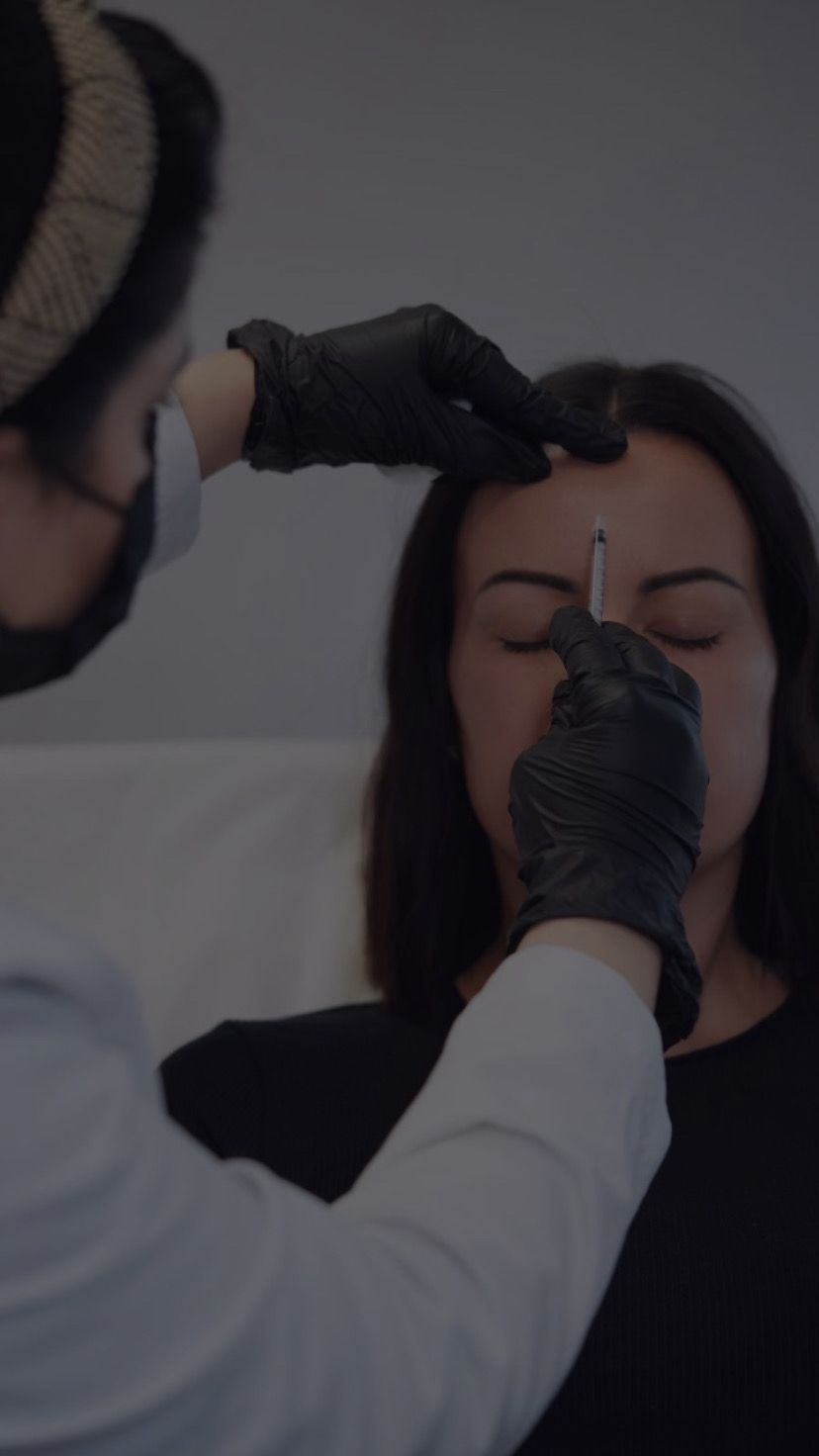 Person getting cosmetic injections in a medical setting; doctor with gloves injecting the forehead.